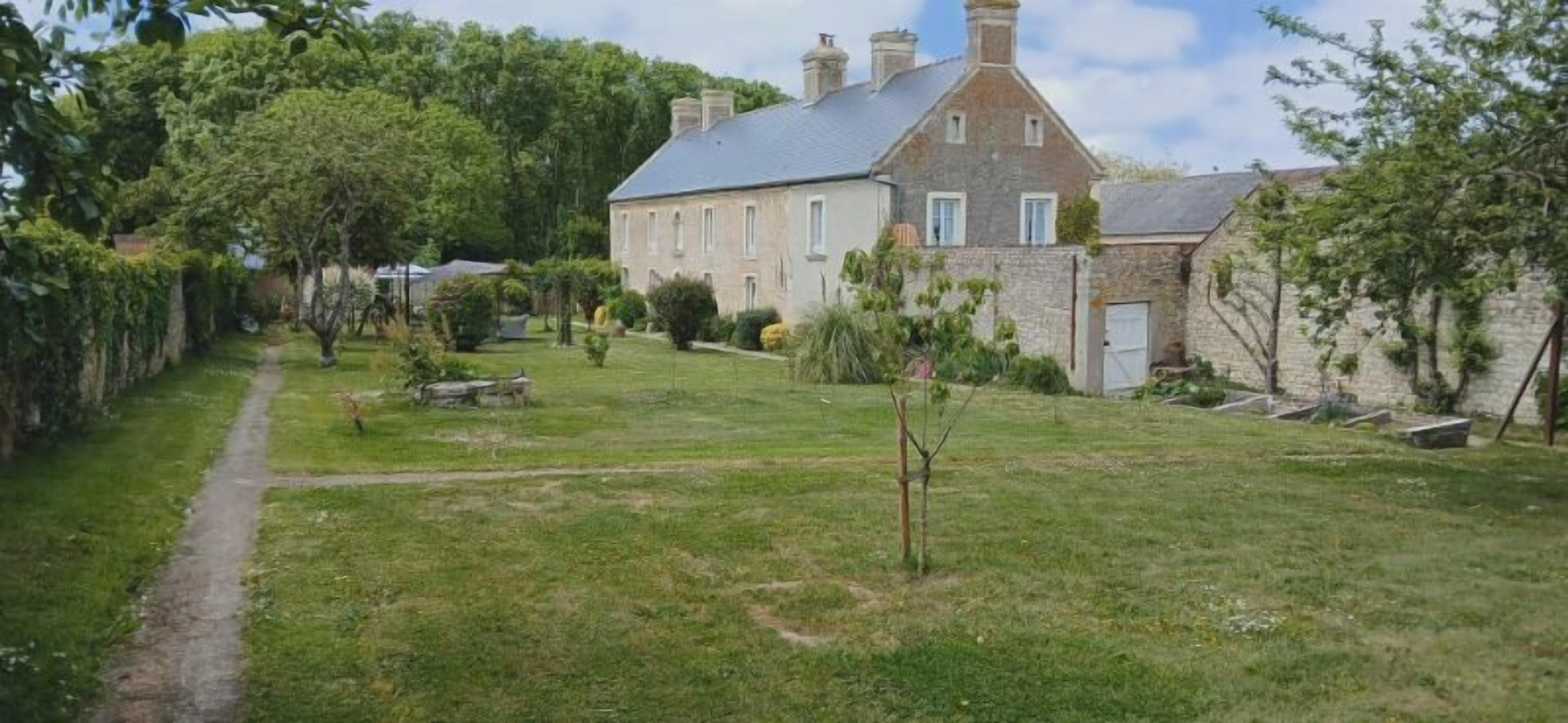 A stone house with a paved path leading to a grassy area with trees and shrubs.