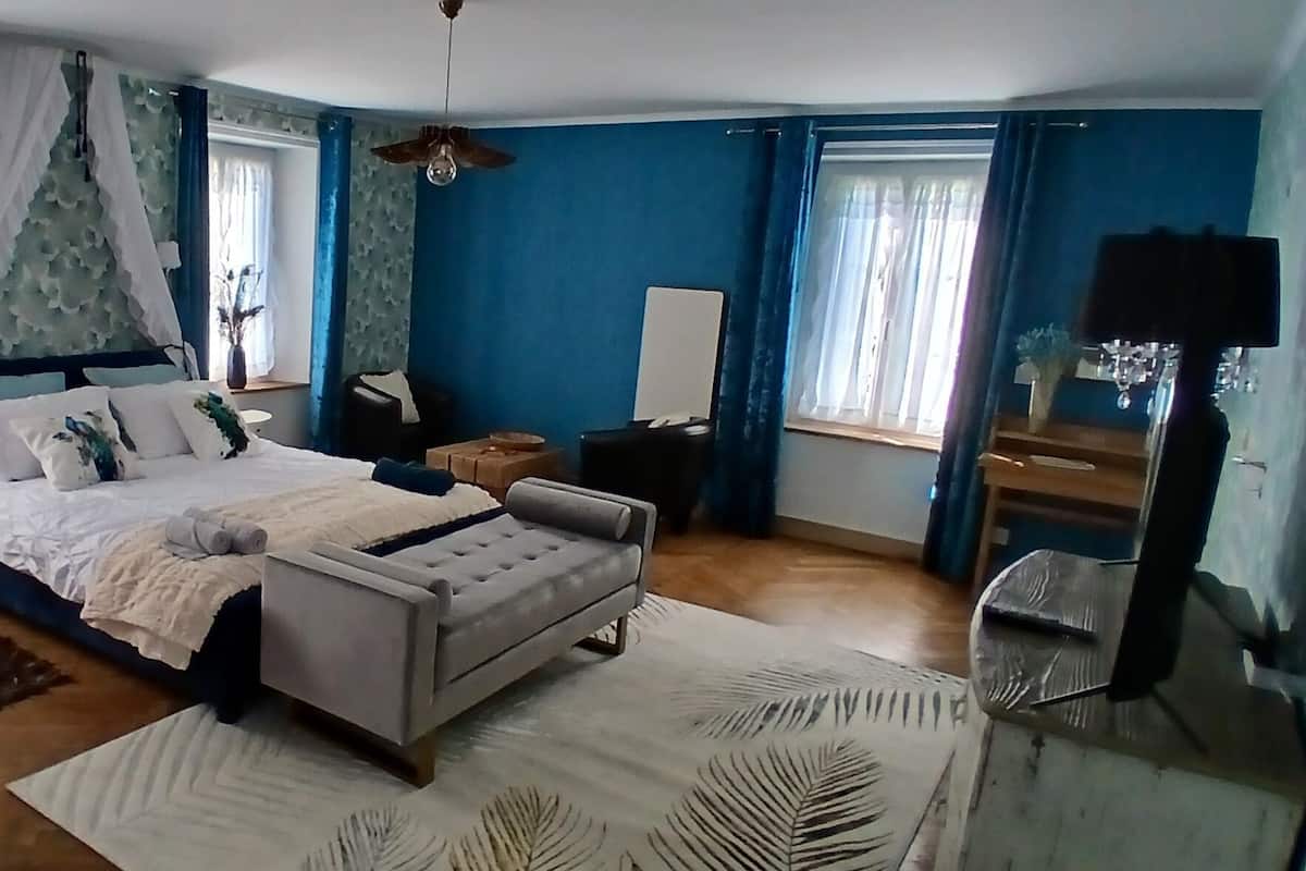 A bedroom with a bed, bedside tables, a nightstand, a chair, and a window with curtains.
