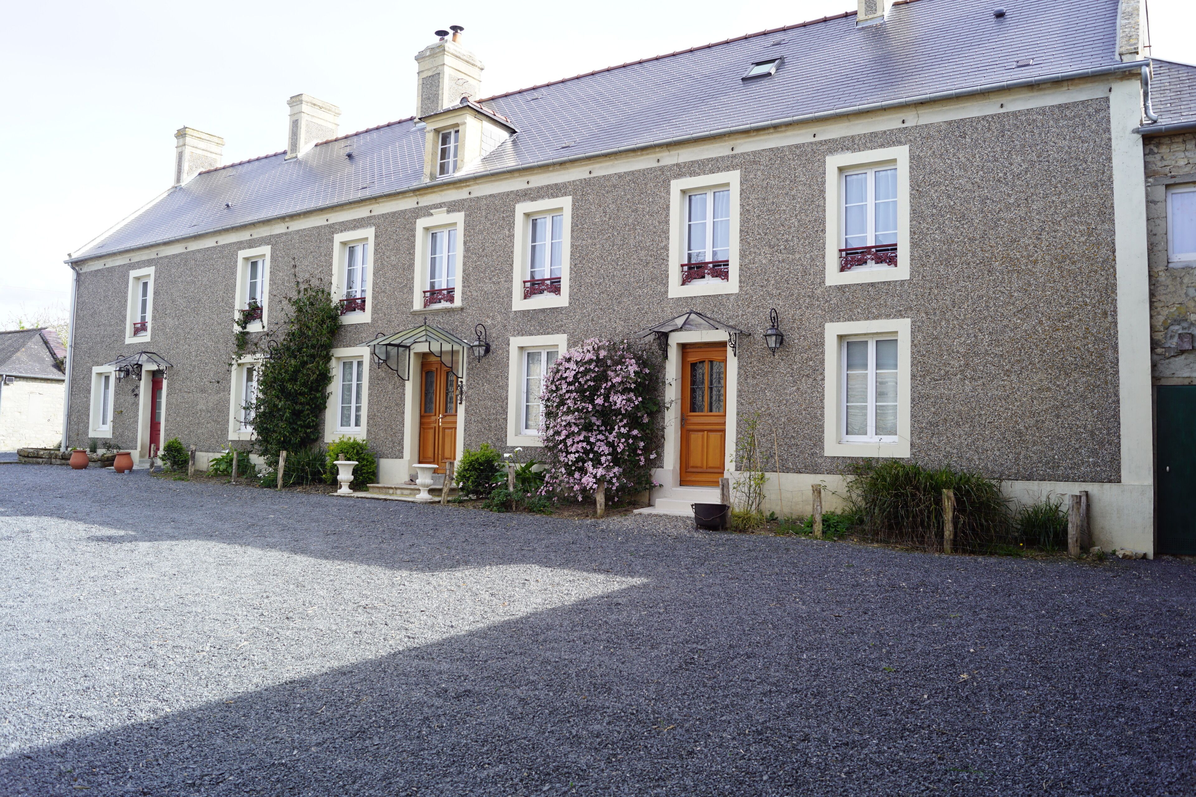 A two-story building with a gravel driveway, multiple windows, and a central entrance with a door and steps.