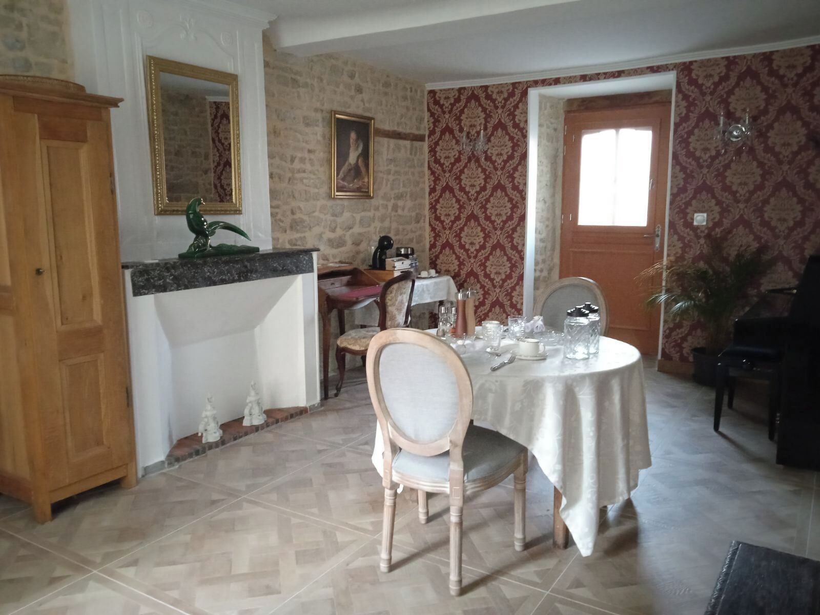 A dining area with a round table set for four, a wooden chair, a cabinet, and a mirror on the wall.