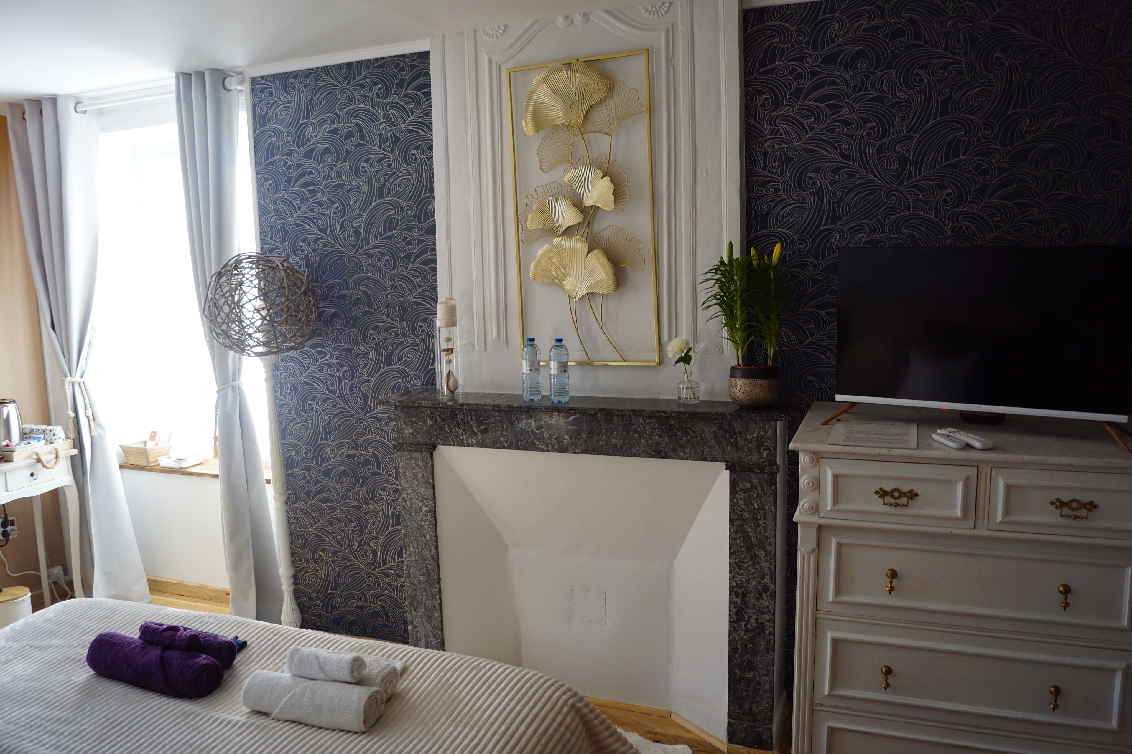 Una habitación de hotel con cama, cómoda, televisor de pantalla plana, un adorno de pared y una planta.