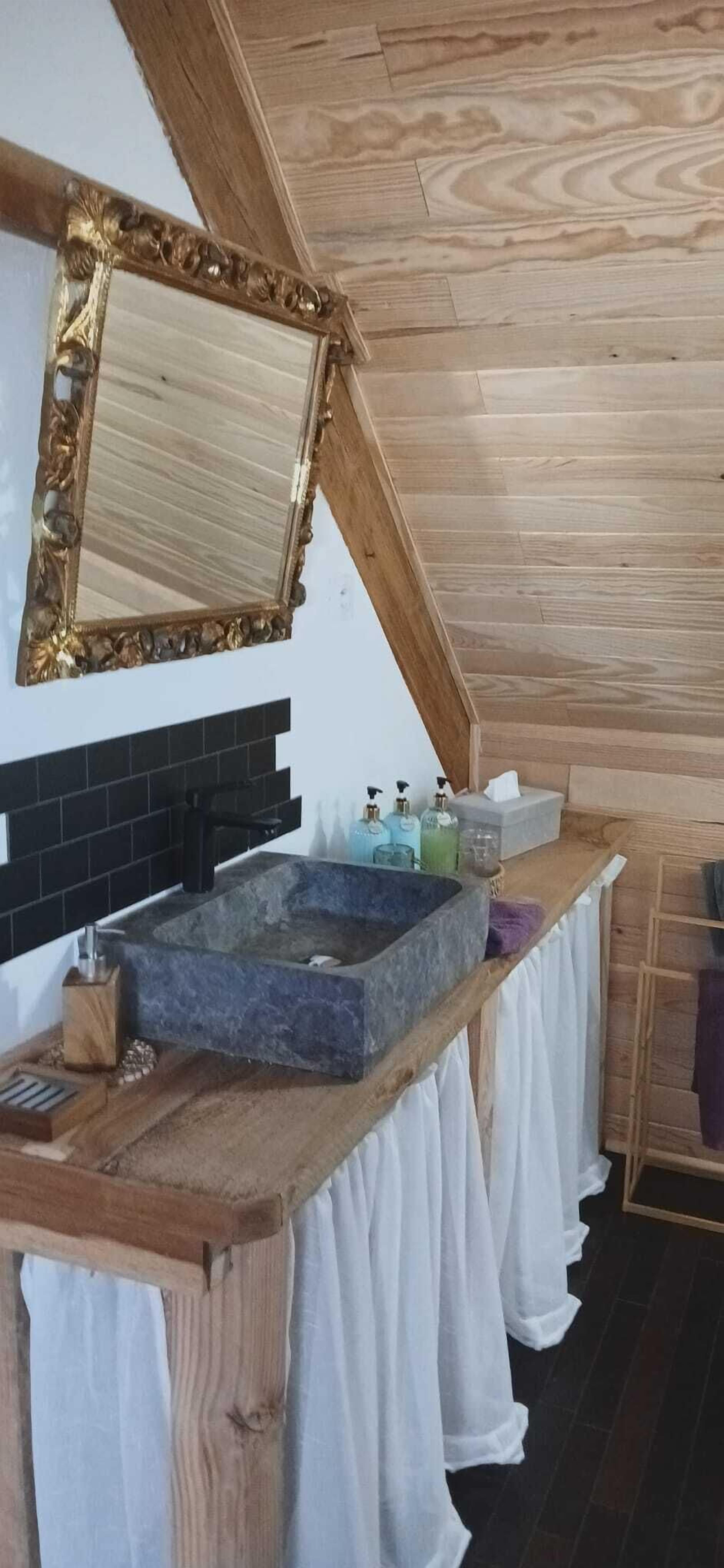 Un baño con un lavamanos de piedra, un espejo con un marco decorativo y un techo de madera.