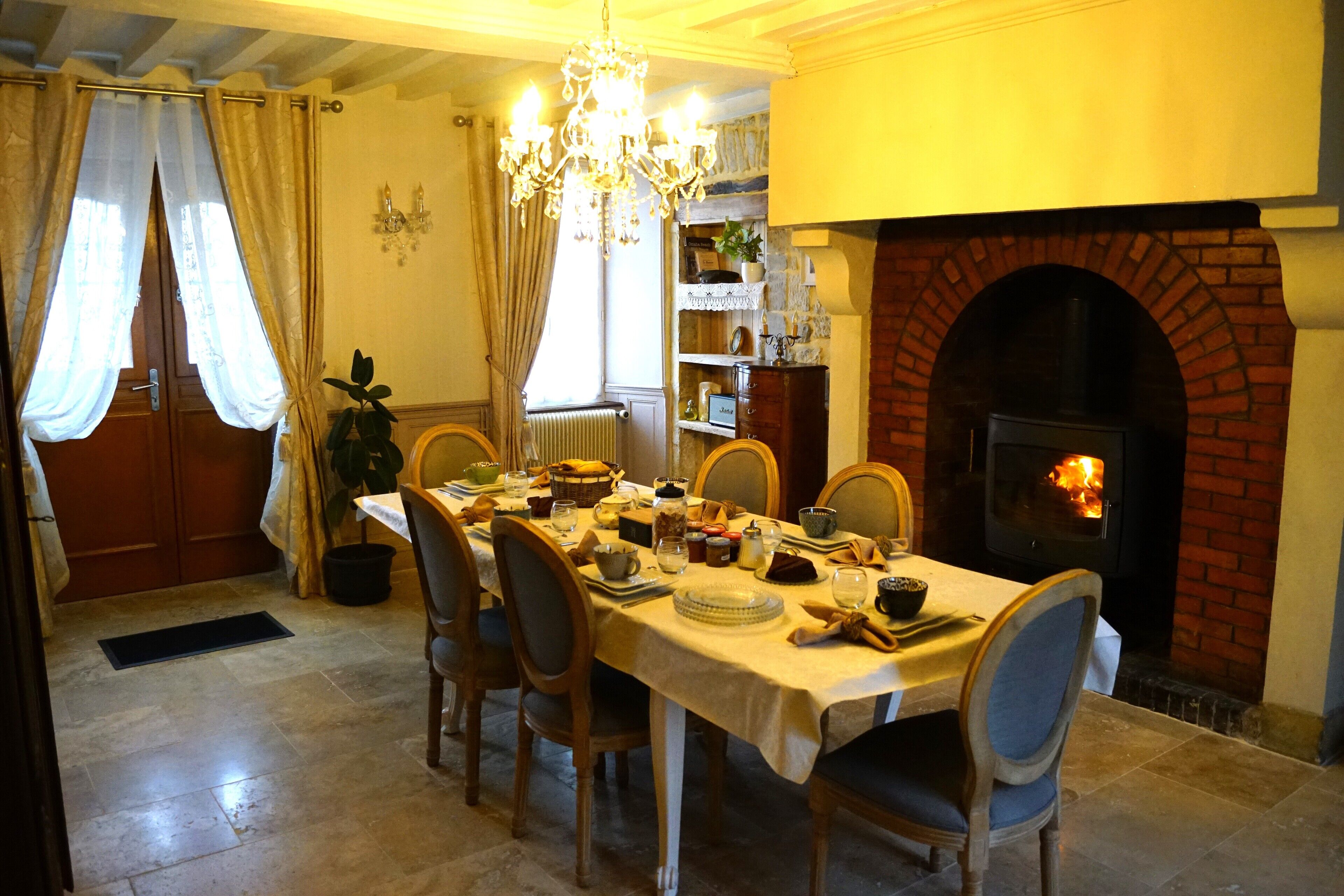 A dining area with a brick fireplace, a chandelier, and a table set for a meal.
