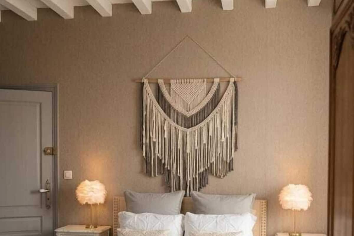 A bedroom with a bed, two bedside tables, a macrame wall hanging, and a wooden ceiling.