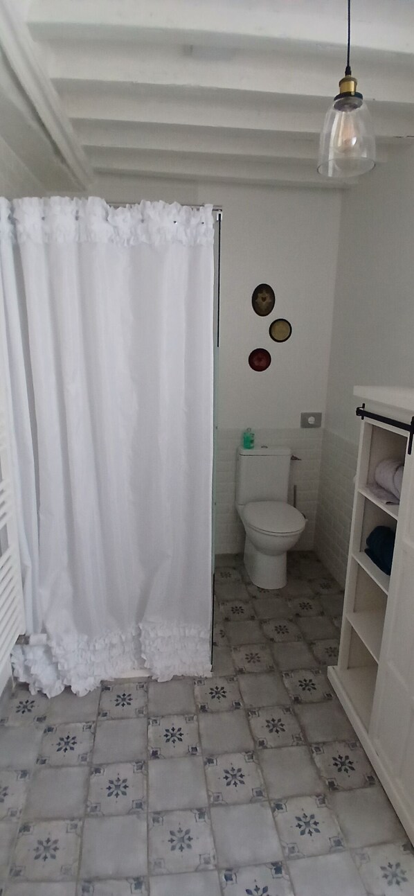 A small, white bathroom with a toilet, a shelf with towels, and a hanging light fixture. - Aux léopards Normands (Mandeville-en-Bessin)