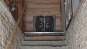 Una escalera de piedra lleva a una habitación con techo de madera y una estatua de Buda.