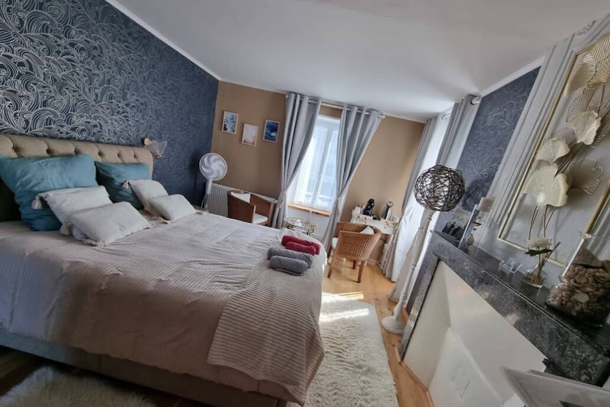 A bedroom with a large bed, a bedside table, a chair, a radiator, and a window with curtains.