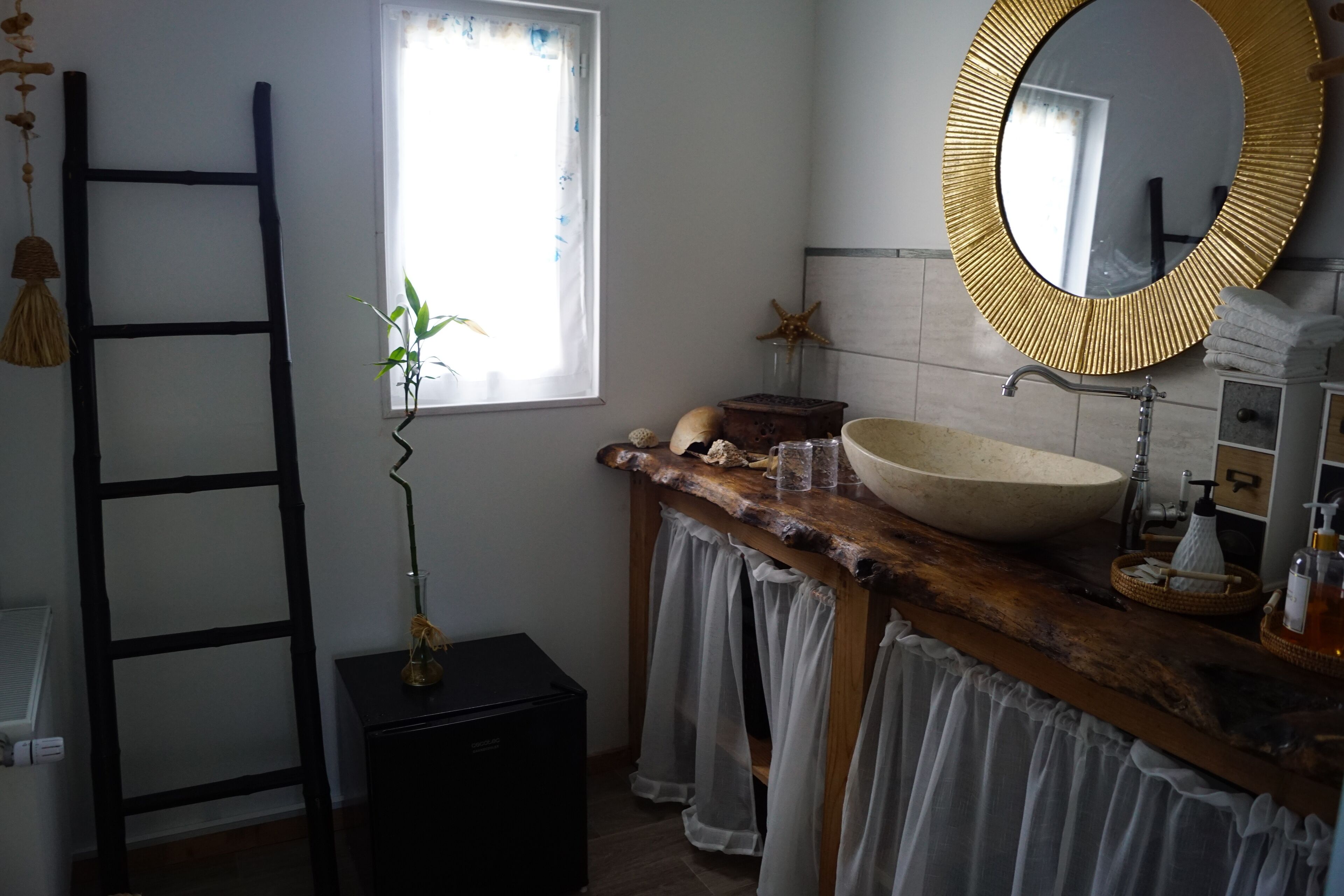 A bathroom with a wooden vanity, a large round mirror, a white sink, and a ladder against the wall.