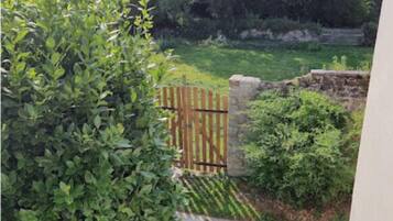 Vista de un jardín con un portón de madera, un muro de piedra y un sendero que lleva a una zona cubierta de césped.