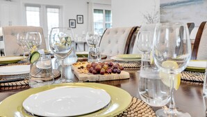 Una mesa de comedor dispuesta con platos, vasos y una tabla de madera con uvas.
