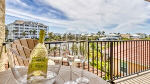 Un balcón con una botella de vino espumoso Moscato, dos copas y una vista despejada de una zona turística con edificios y palmeras.