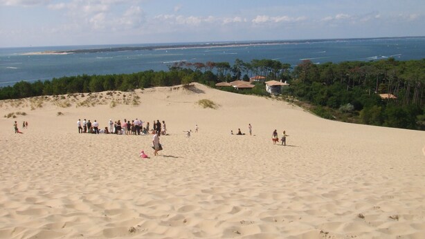 A sandy beach with a group of people, a clear sky, and a view of the sea and distant coastline.