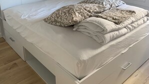 A neatly made bed with a patterned pillow and a folded blanket, a bedside table with a lamp, and a white wardrobe.