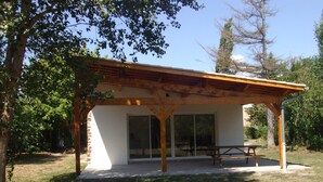 A covered outdoor area with a picnic table and benches, surrounded by trees and a clear sky.