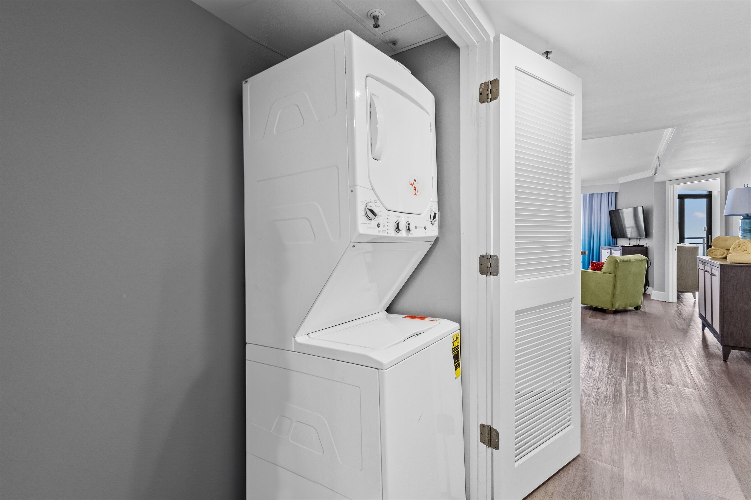 A modern laundry room with a large white washer and dryer, a door leading to a living area with a television and seating.