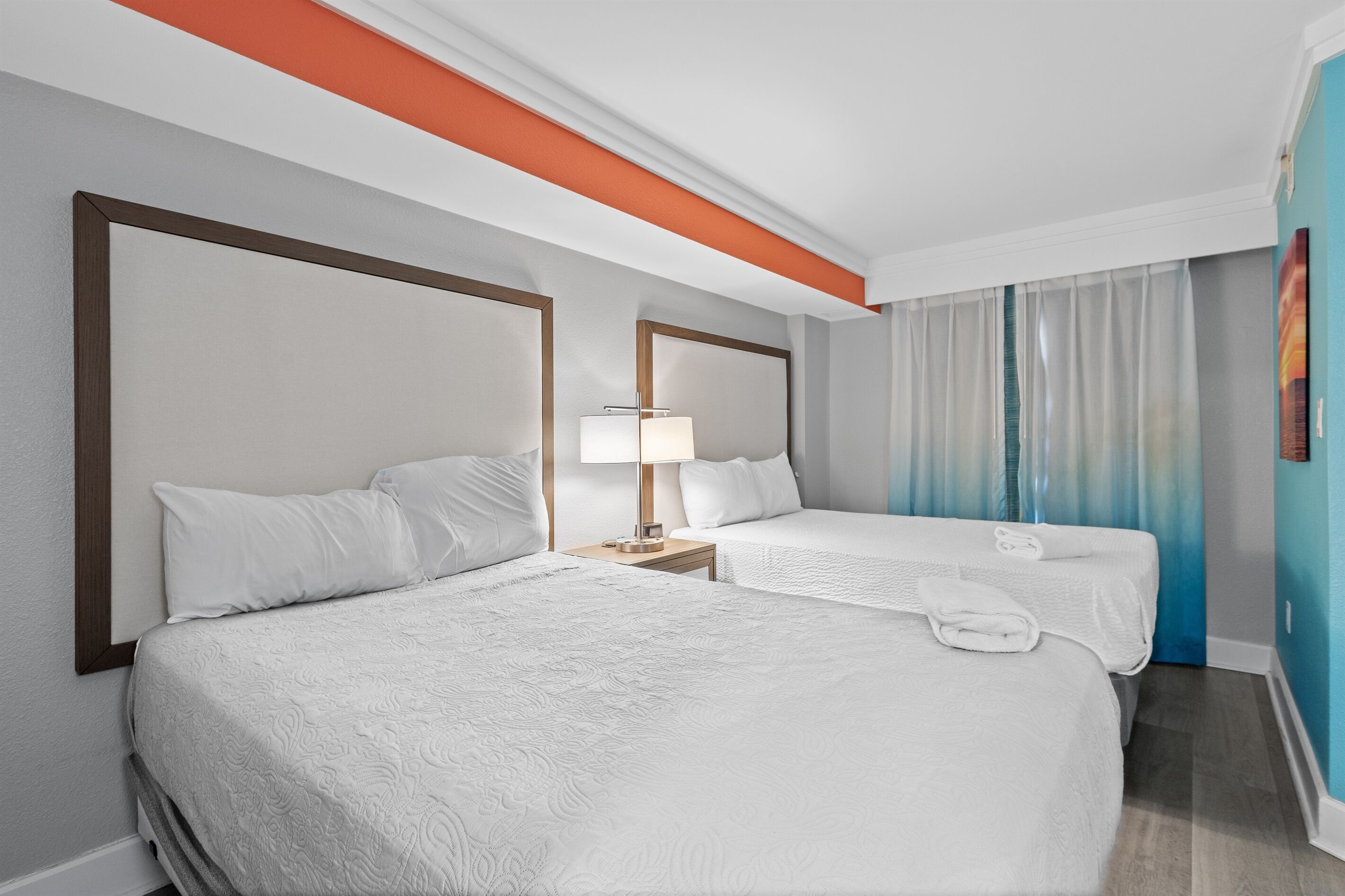 A hotel room with two beds, a nightstand with a lamp, and a window with curtains.