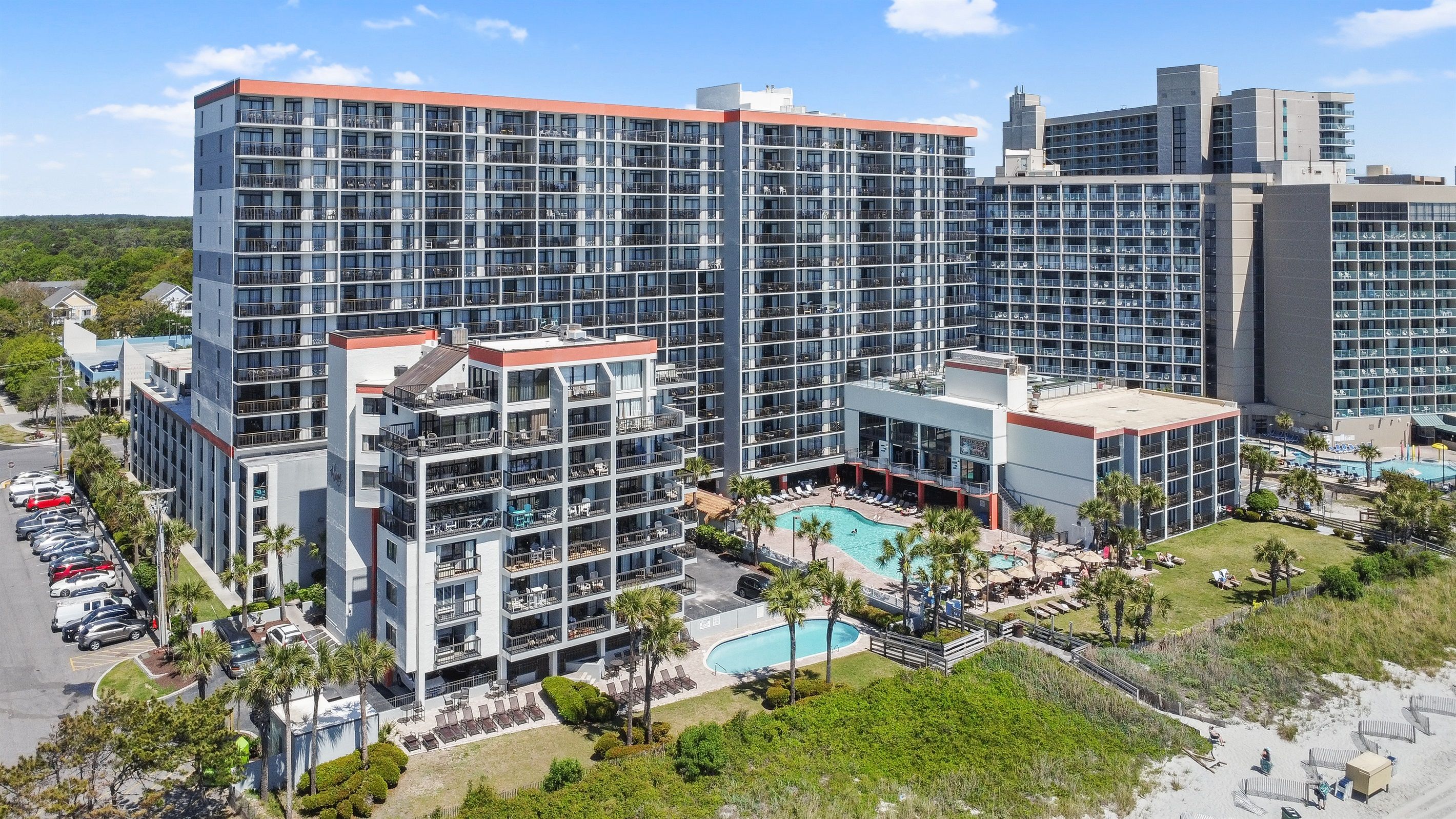 A high-rise hotel with multiple balconies, a swimming pool, and a landscaped poolside area.