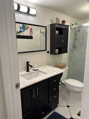 Een badkamer met een wit wastafel, zwarte kastjes, een toilet en een douche.