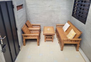 A small, enclosed outdoor seating area with a table and two wicker sofas, a door, and a window with a metal grill. - Esperanza (Abomey-Calavi)
