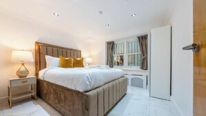 A bedroom with a large bed, a bedside table with a lamp, a window with curtains, and a wardrobe. - The Paddington Residences (London)