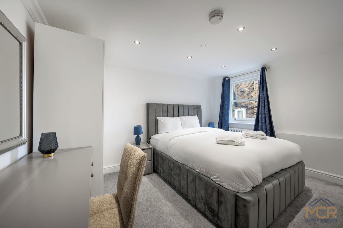 Une chambre d’hôtel moderne avec un grand lit, une table de chevet, une chaise et une fenêtre avec des rideaux.