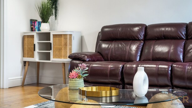 A modern living room with a leather sofa, a glass coffee table, and a white console unit with shelves. - The Paddington Residences (London)