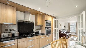A modern kitchen with wooden cabinets, stainless steel appliances, and a dining area with a glass table and chairs. - The Paddington Residences (London)