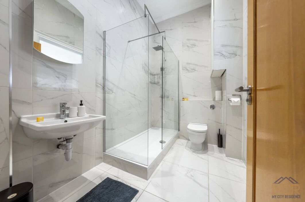Un bagno moderno con doccia vetro e accessori, lavabo con articoli da toilette e water.