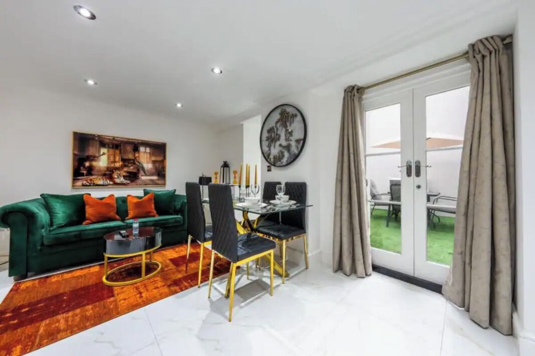 Uma sala de estar moderna com um sofá verde, uma mesa de jantar com cadeiras e uma janela grande com cortinas.