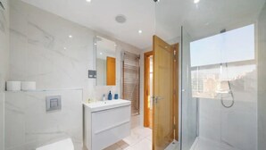 A modern bathroom with a toilet, vanity, and glass shower enclosure. - The Paddington Residences (London)