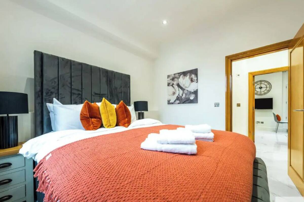 Une chambre à coucher moderne avec un grand lit, une tête de lit, des tables de chevet et un tableau au mur.