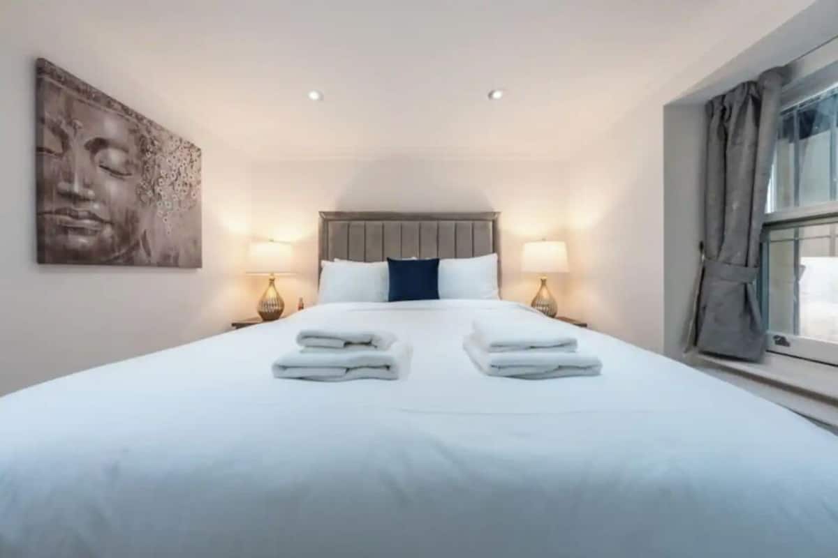 Une chambre d’hôtel avec un grand lit, deux lampes de chevet, une œuvre d’art accrochée au mur et une fenêtre avec des rideaux.