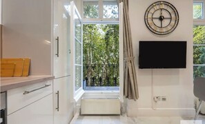 A modern kitchen with white cabinets, a built-in oven, and a window with a view of trees. - The Paddington Residences (London)
