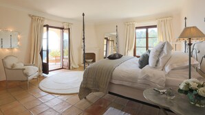 Une chambre avec un grand lit, une chaise, un tapis rond et une table sur laquelle se trouvent une lampe et des fleurs.