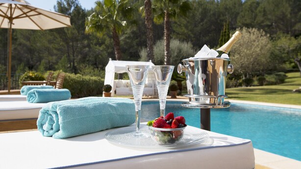 Une table au bord de la piscine, avec une bouteille de champagne, deux verres et un saladier de fruits.