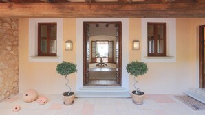Une entrée de bâtiment de style traditionnel, avec un plafond en poutres apparentes, deux plantes en pot et un sol carrelé.