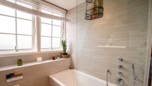 Un baño moderno con bañera, ducha y ventana con persianas.