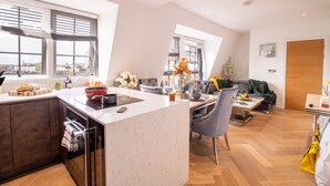 Una cocina moderna con una isla central, un área de comedor con sofá y ventanas amplias que ofrecen vista a la ciudad.
