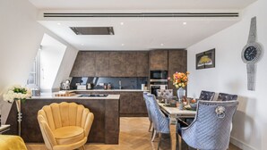 Una cocina moderna con armarios oscuros, una isla central y un comedor con una silla amarilla y una silla azul acolchada.