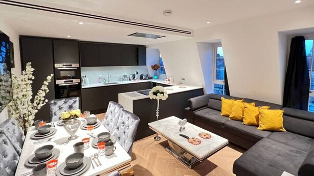 Ein modernes Wohnzimmer mit Essbereich, einer gelb gepolsterten Couch und einer Küche im Hintergrund.