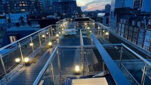 Eine moderne Dachterrasse in der Stadt mit Glasgalerie, Metallgeländern und einer Treppe zu einer erhöhten Ebene.