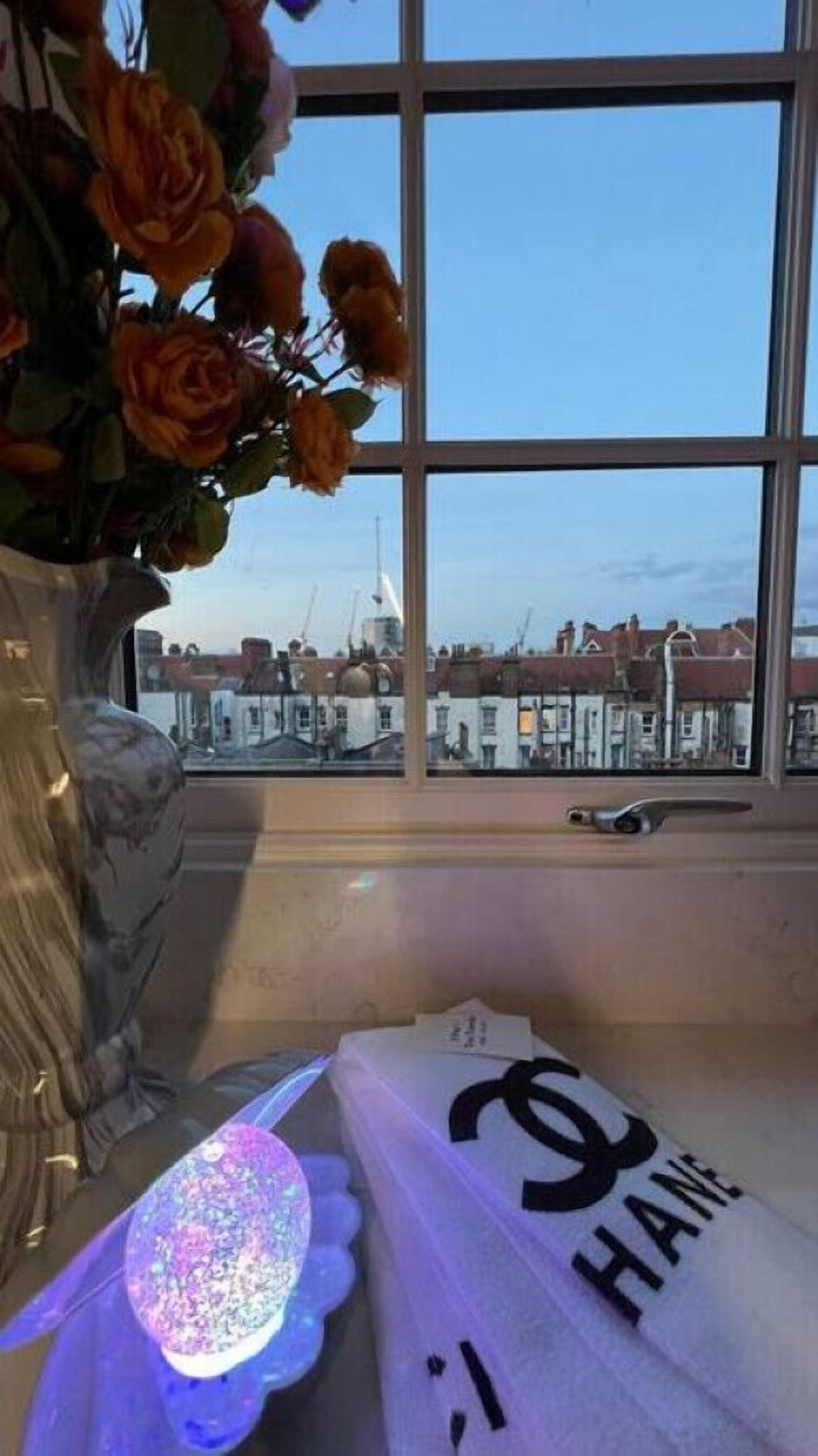 Quarto com uma grande janela, um vaso com flores e uma cama com cobertor.