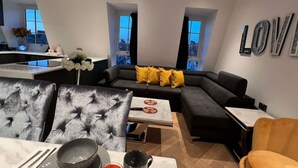 Ein modernes Wohnzimmer mit Sofa, Esstisch und Küchenzeile mit Fenster.