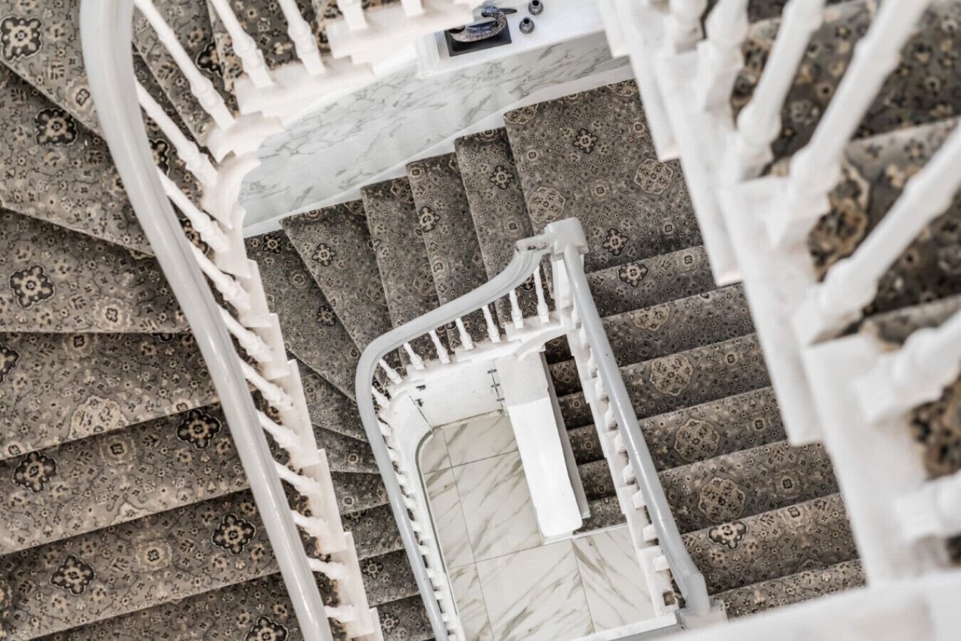 A spiral staircase with a patterned carpet and white railings.
