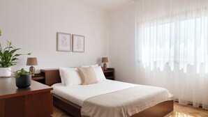 Ein ordentlich eingerichtetes Schlafzimmer mit Bett, Nachttischen, einer Lampe, einer Topfpflanze und gerahmten Bildern an der Wand.