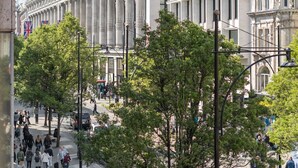 Blick auf eine Straße mit einer Reihe klassischer Gebäude, einige mit gelben Flaggen, und Fußgängern auf dem Bürgersteig.