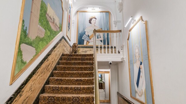 Un magnifique escalier, avec des marches recouvertes d’une moquette richement décorée, menant à un balcon.
