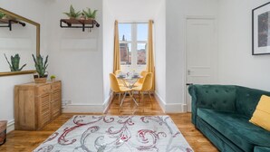 Une pièce comprenant un coin repas, un canapé vert, un meuble en bois et une fenêtre avec des rideaux.