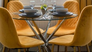 Une table à manger, dressée pour quatre personnes, avec des chaises, placée devant une fenêtre ornée de rideaux.