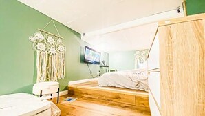 Een kleine, gezellige kamer met een lage balken plafond, een bed met een witte matras en een houten hoofdeinde, een klein krukje en een dreamcatcher aan de muur.